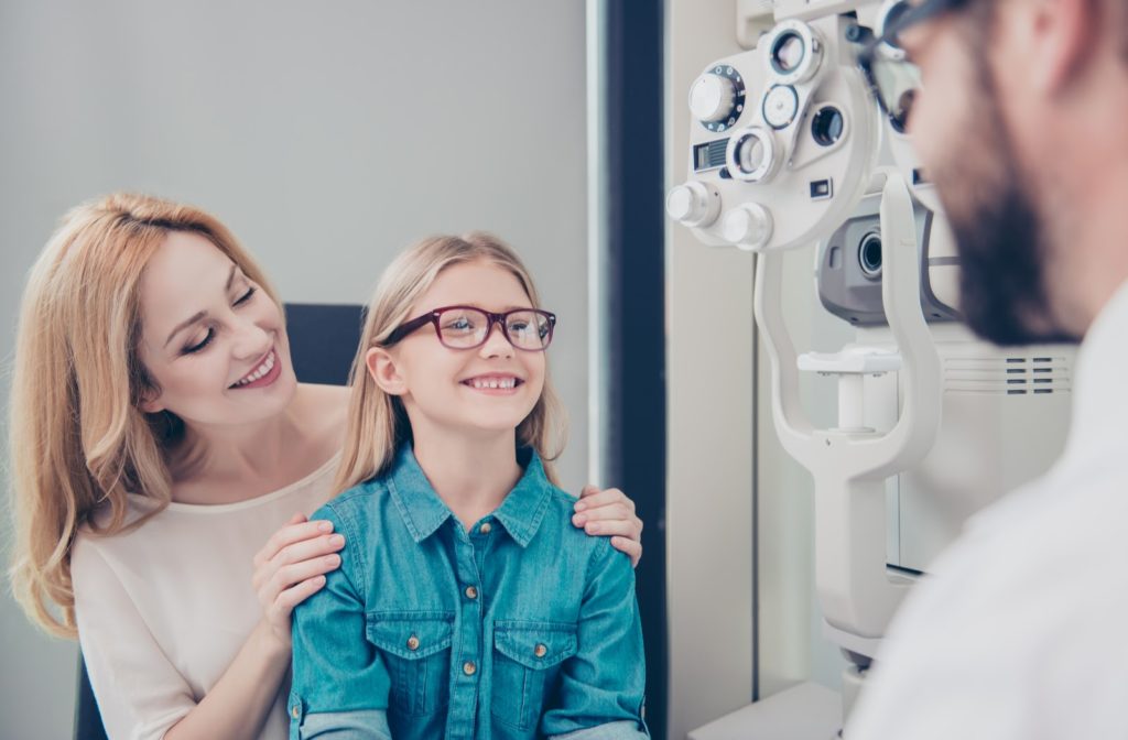 Smiling young girl with her mother at the optometrist trying on glasses