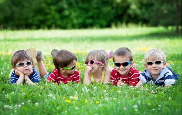 Five kids laying outside on the grass wearing sunglasses to protect their eyes from the sun and slowing the possible progression of myopia