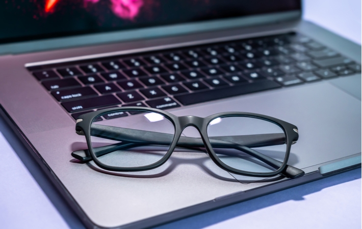 A pair of blue light glasses with black frames, resting on the keyboard of a laptop