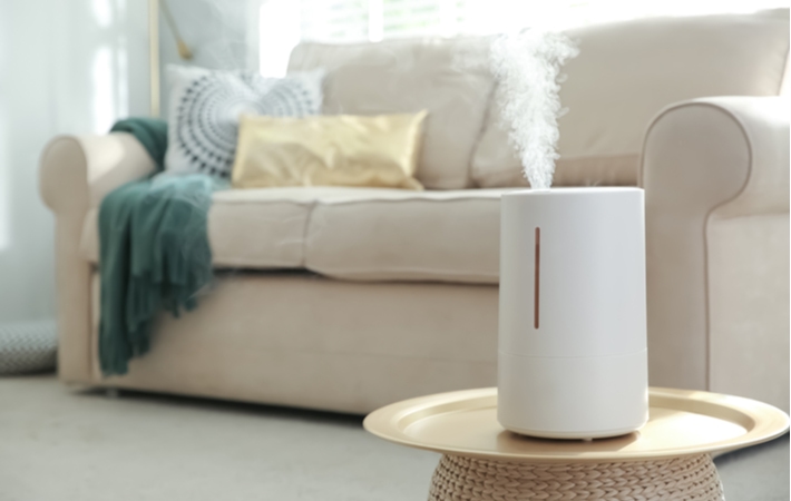 A white humidifier set up on a small stand in a living room with a blurred couch in the background