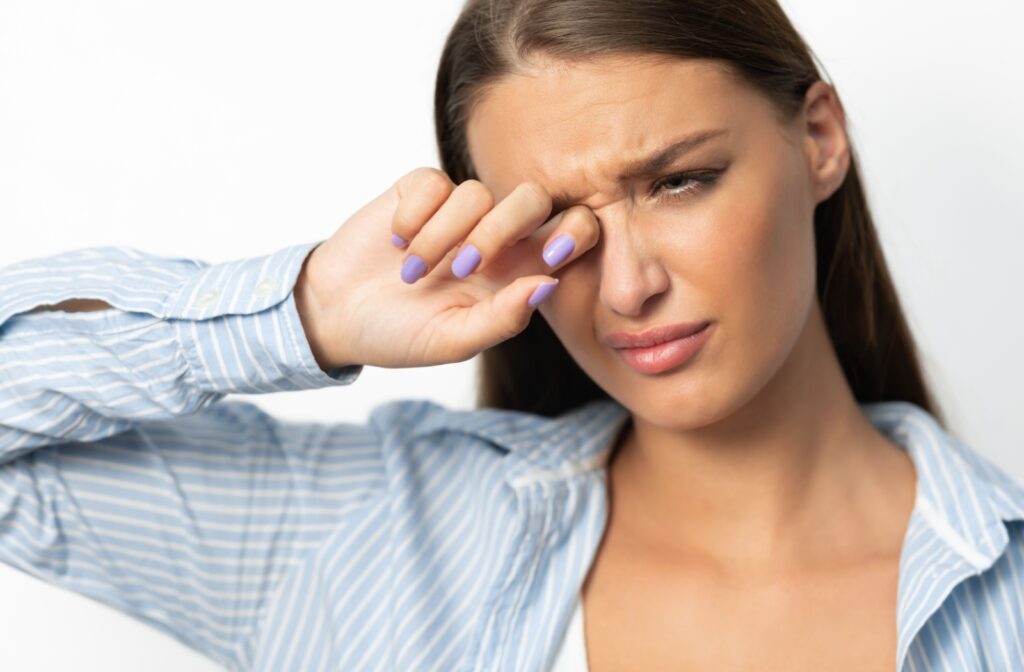  A young woman rubs her eye with her finger, due to a possible eyelash in her eye.