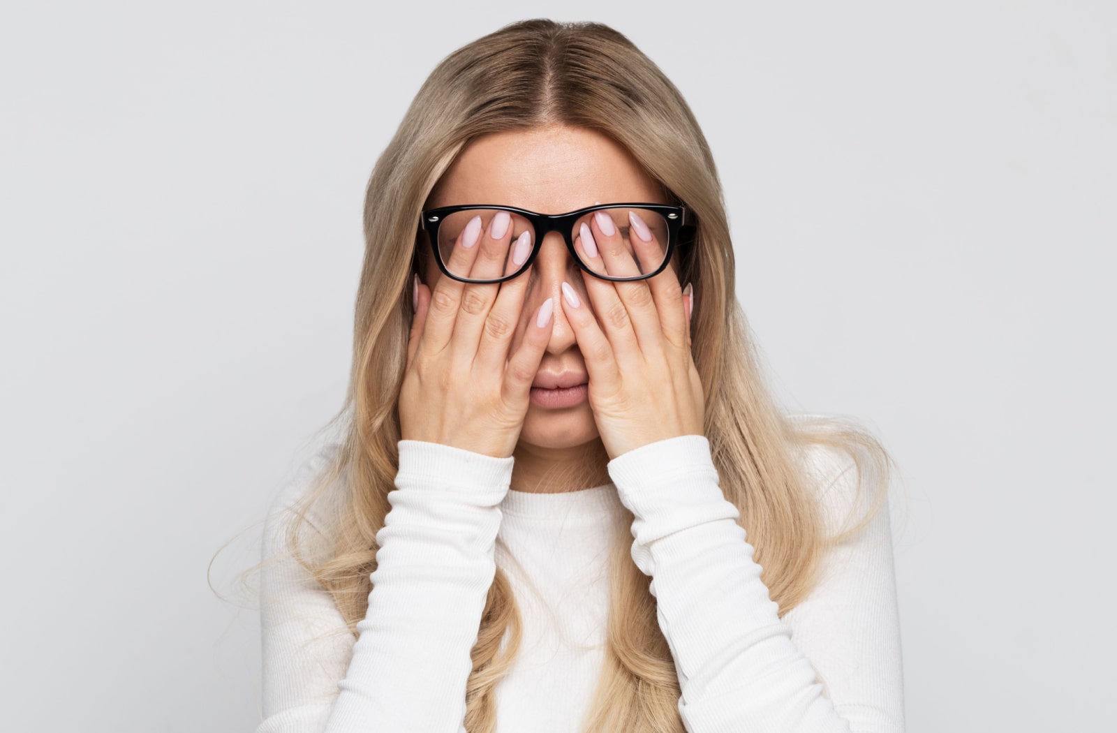 A woman covering her eyes with her hands underneath her glasses