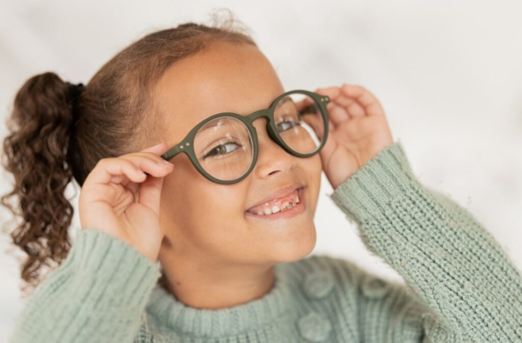 A young girl in glasses smiling and holding the arms on the eyeglasses frames