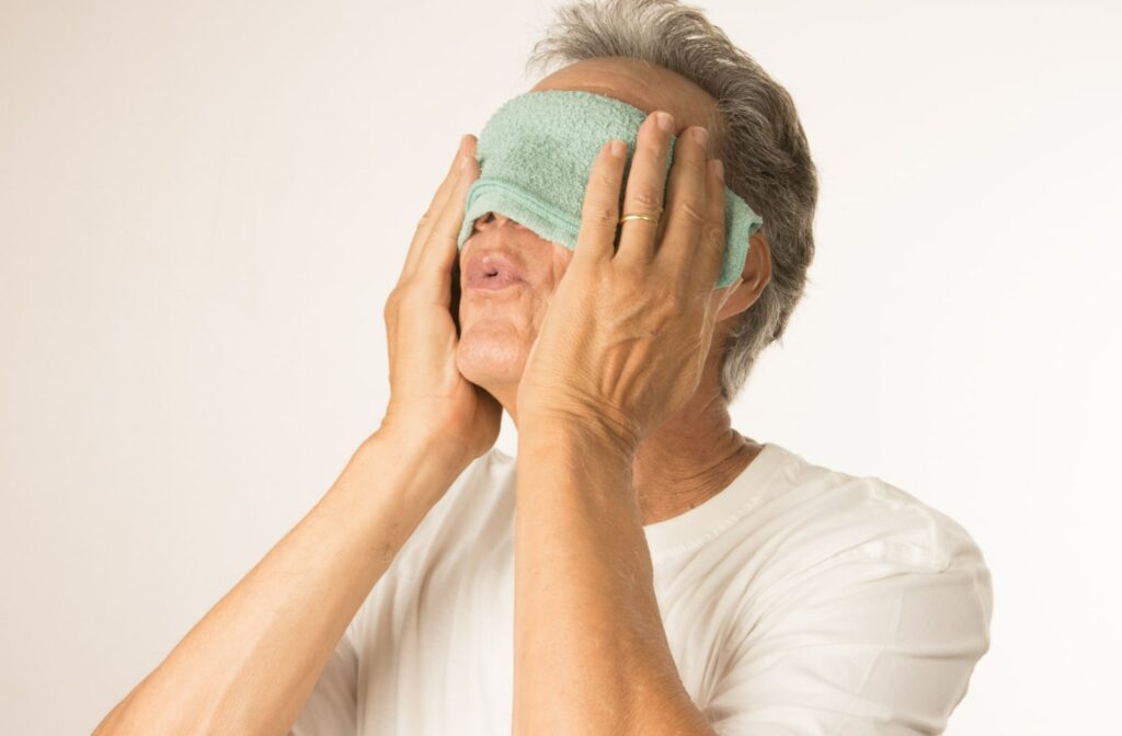 A male patient using a warm compress over his eyes to relieve discomfort.