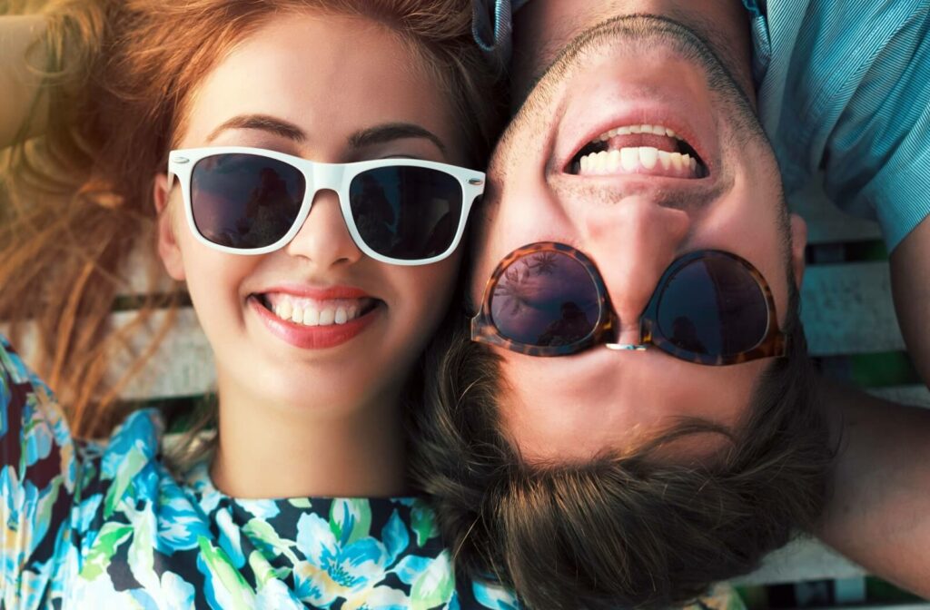 Two people laying with their heads together, both smiling and wearing sunglasses.