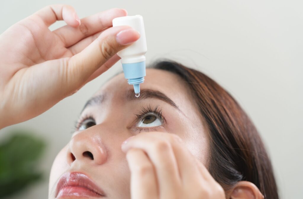 A woman is using eye drops She is holding one eye open and looking up while she squeezes the eye drop bottle with the other hand.