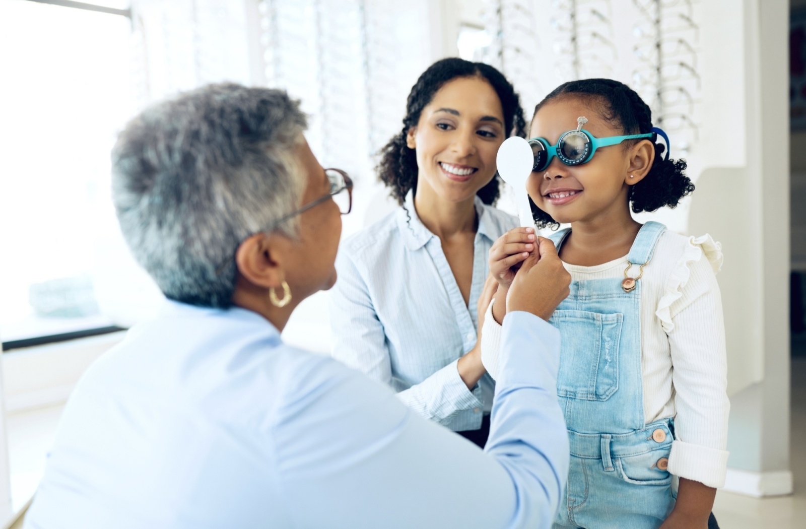 A smiling child undergoes visual acuity testing as their parent gently reassures them.