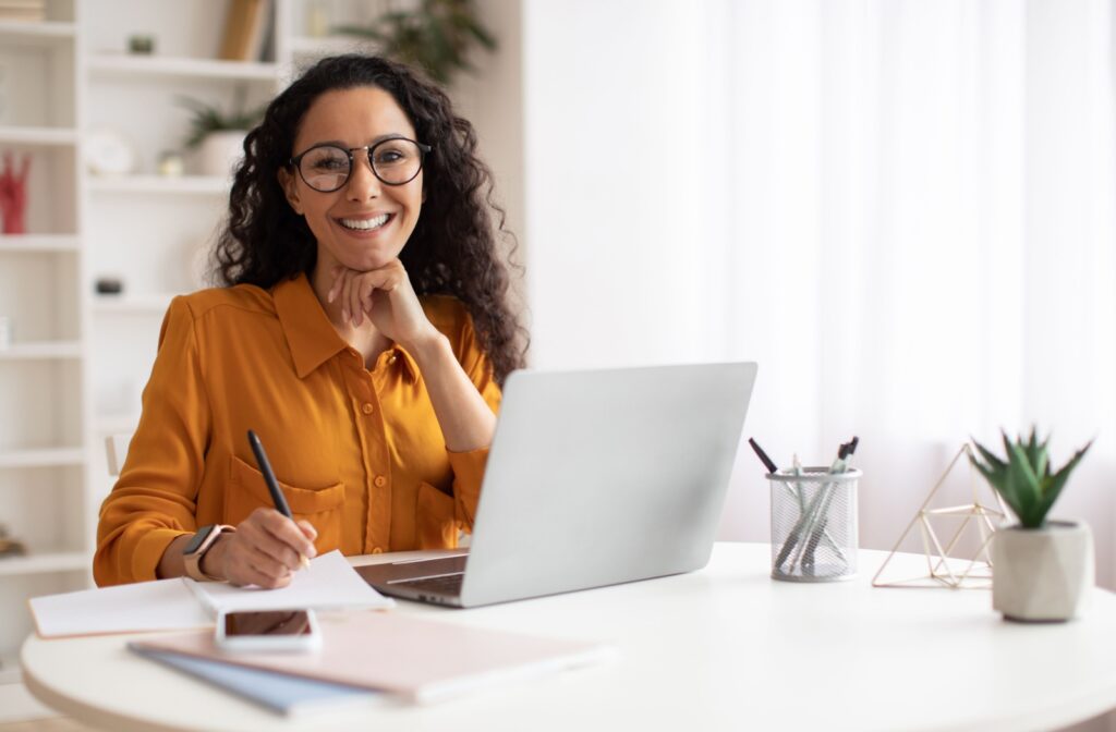 A person working at a desk, switching between a computer, handwritten notes, and a phone. Their multifocal glasses help them see clearly at different distances, making it easier to handle both close-up and far-away tasks.